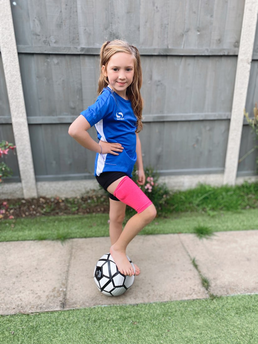 Girl with soccer ball wearing pink heathered support sleeve on leg