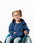 Young girl in a wheelchair wearing a blue Zipper Access hoodie on a white background
