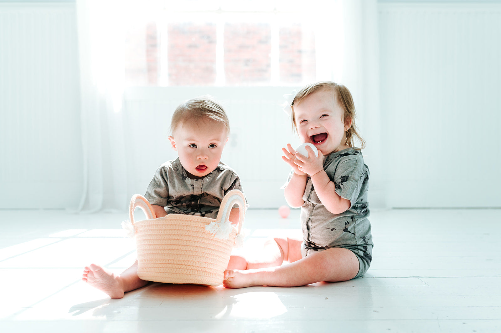 Two babies sitting in white room wearing all access bodysuits