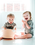 Two babies sitting in white room wearing all access bodysuits