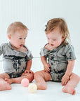 Two babies sitting in white room in all access bodysuits
