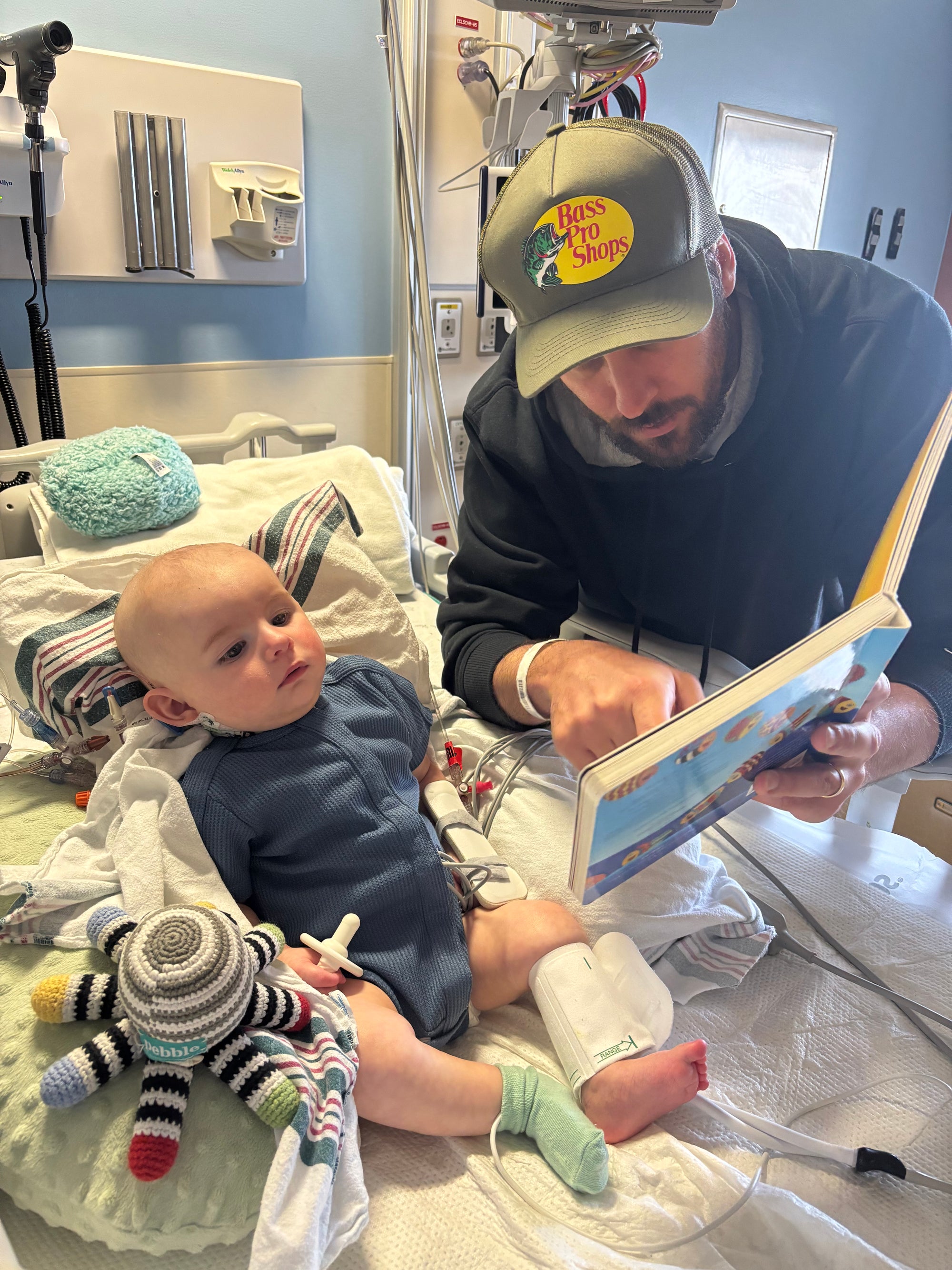 Baby in blue waffle all access bodysuit with dad reading to him