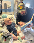 Baby in blue waffle all access bodysuit with dad reading to him