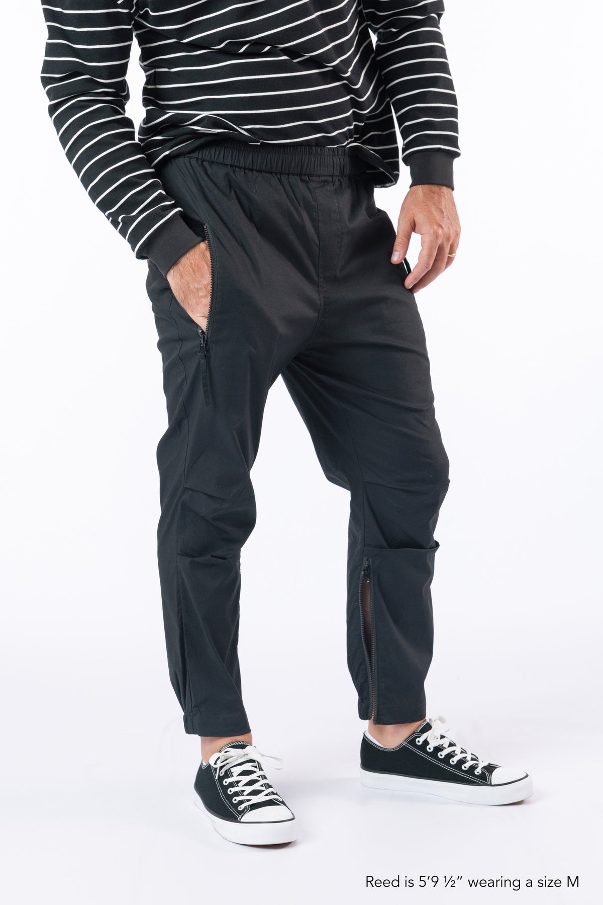Male model wearing black casual zip pants with hand in pocket