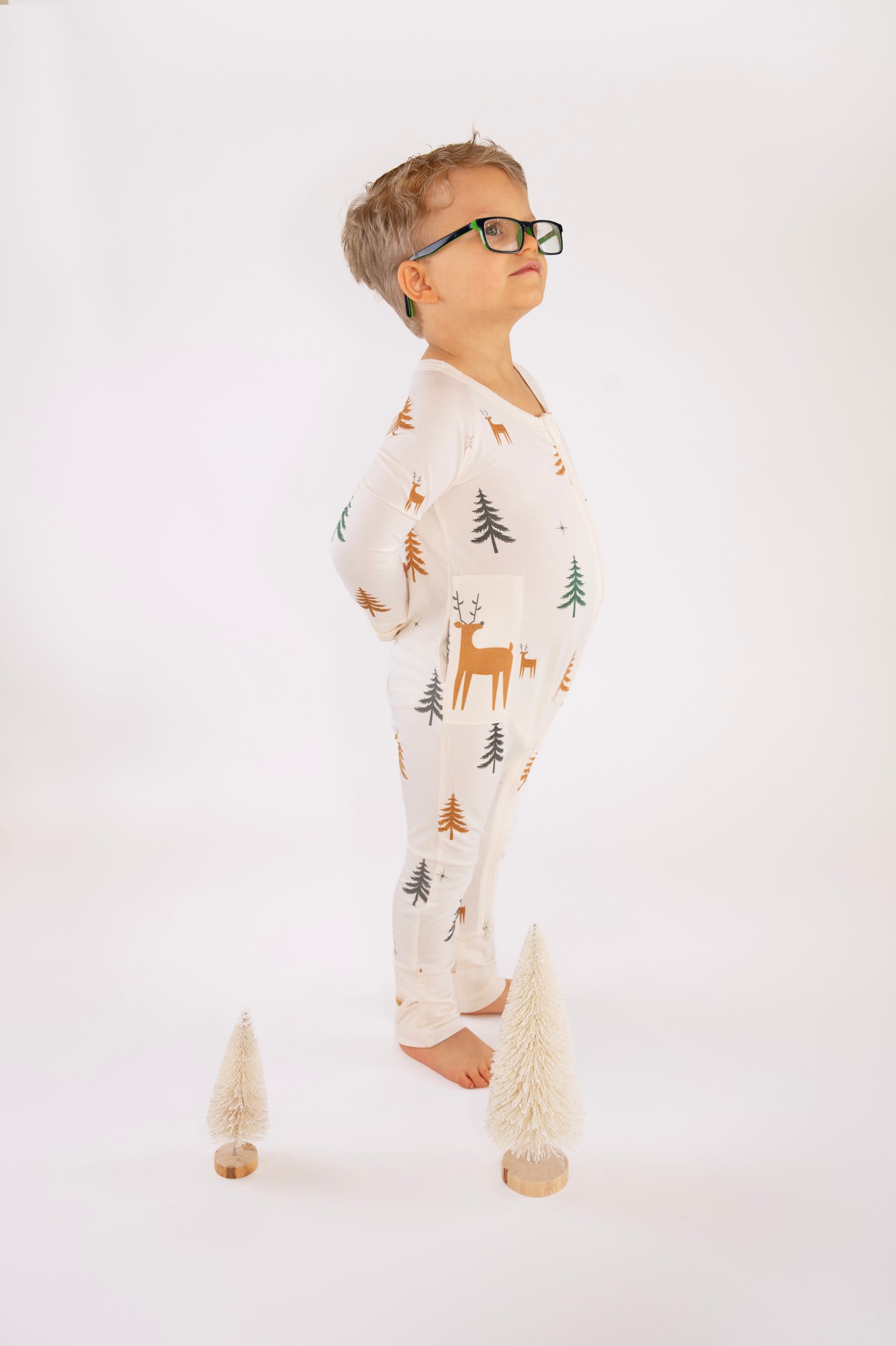 Boy standing in Thru the Trees G-Tube Pajamas with mini tree decorations