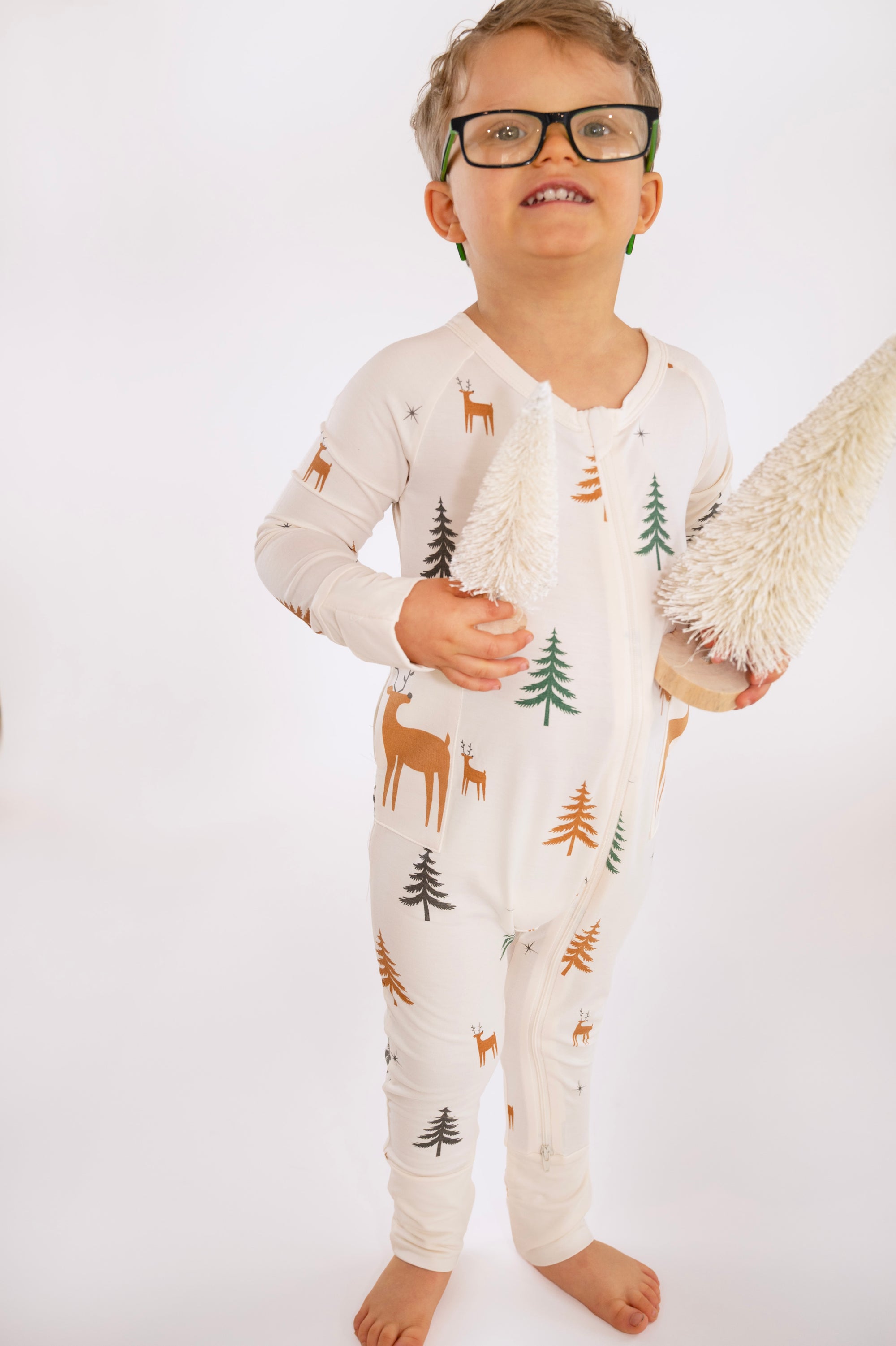 Child standing wearing Thru the Trees G-Tube Pajamas, holding mini tree decorations