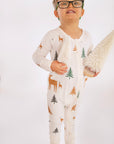 Child standing wearing Thru the Trees G-Tube Pajamas, holding mini tree decorations