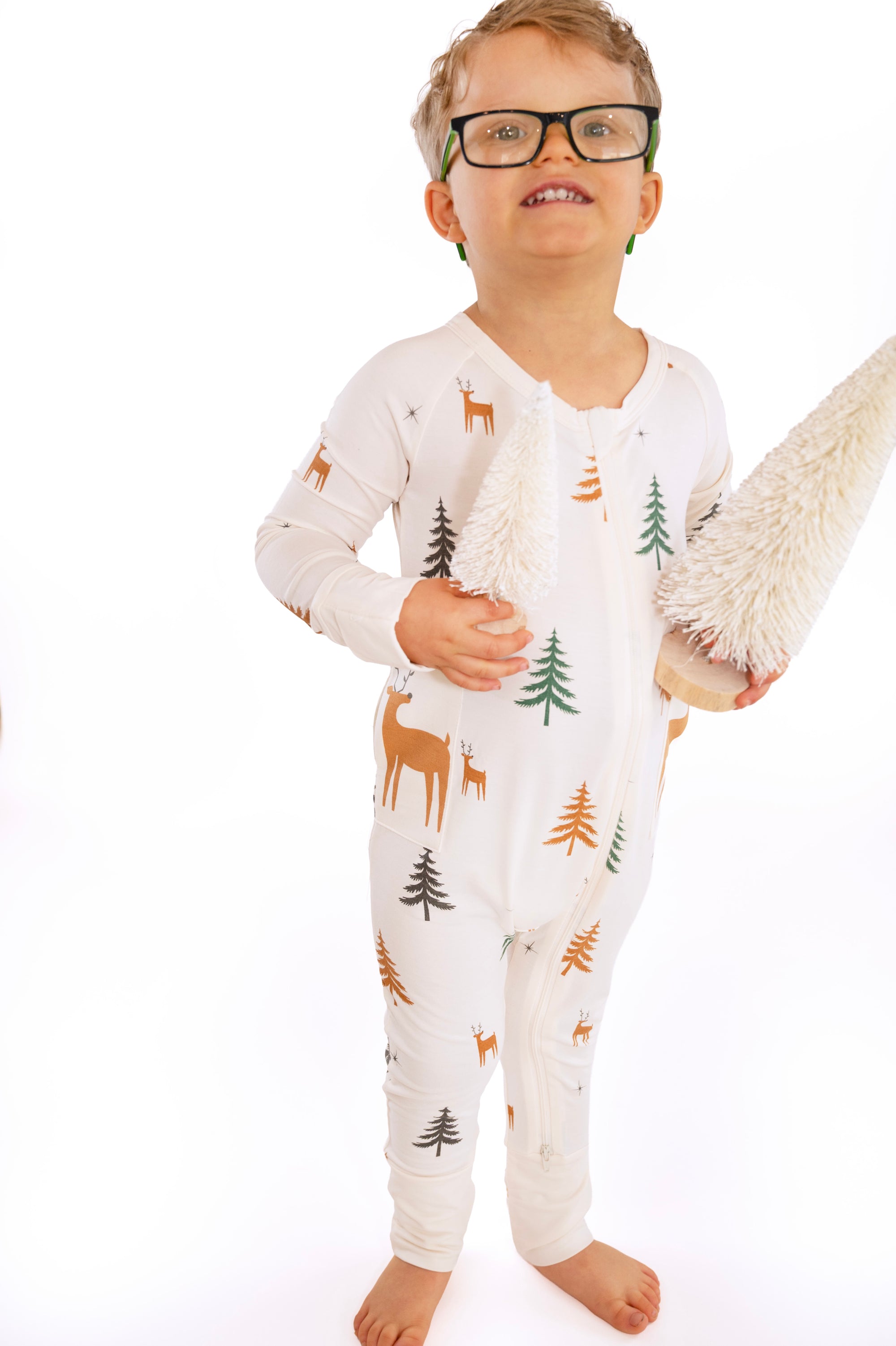 Child standing wearing Thru the Trees G-Tube Pajamas, holding mini tree decorations
