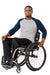 A smiling man in a gray and navy raglan long-sleeve shirt and black pants sits in a manual wheelchair against a plain white background.