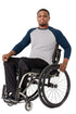 A smiling man in a gray and navy raglan long-sleeve shirt and black pants sits in a manual wheelchair against a plain white background.