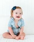 Baby girl wearing an adaptive baby bodysuit. The front is partially unsnapped, showing the front plastic snap panel.