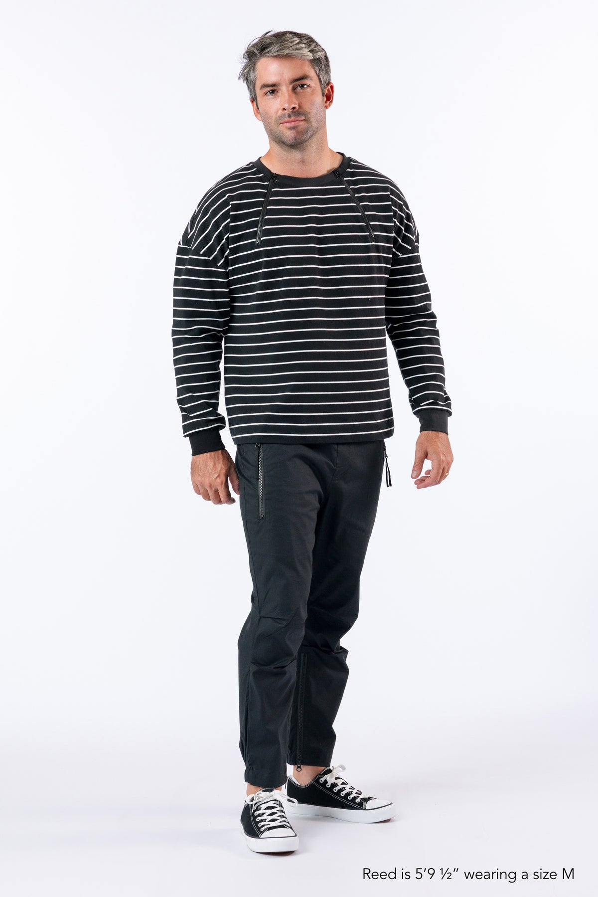 Man wearing Chest Zip Access tee and casual zip pants. Text reads "Reed is 5'9 1/2" wearing a size M".