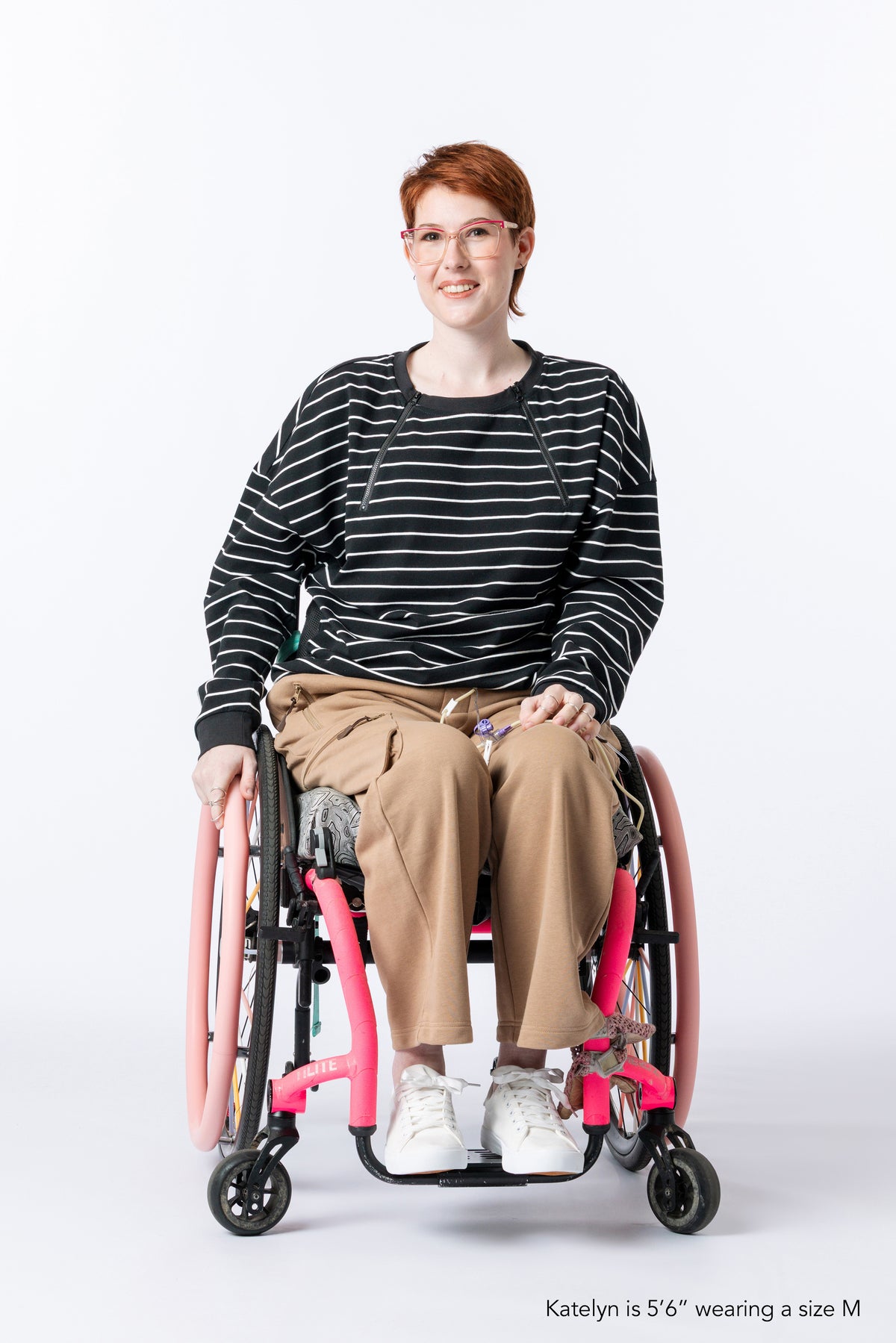 Woman in wheelchair wearing Chest Zip Access Tee. Text reads "Katelyn is 5'6" wearing a size M".