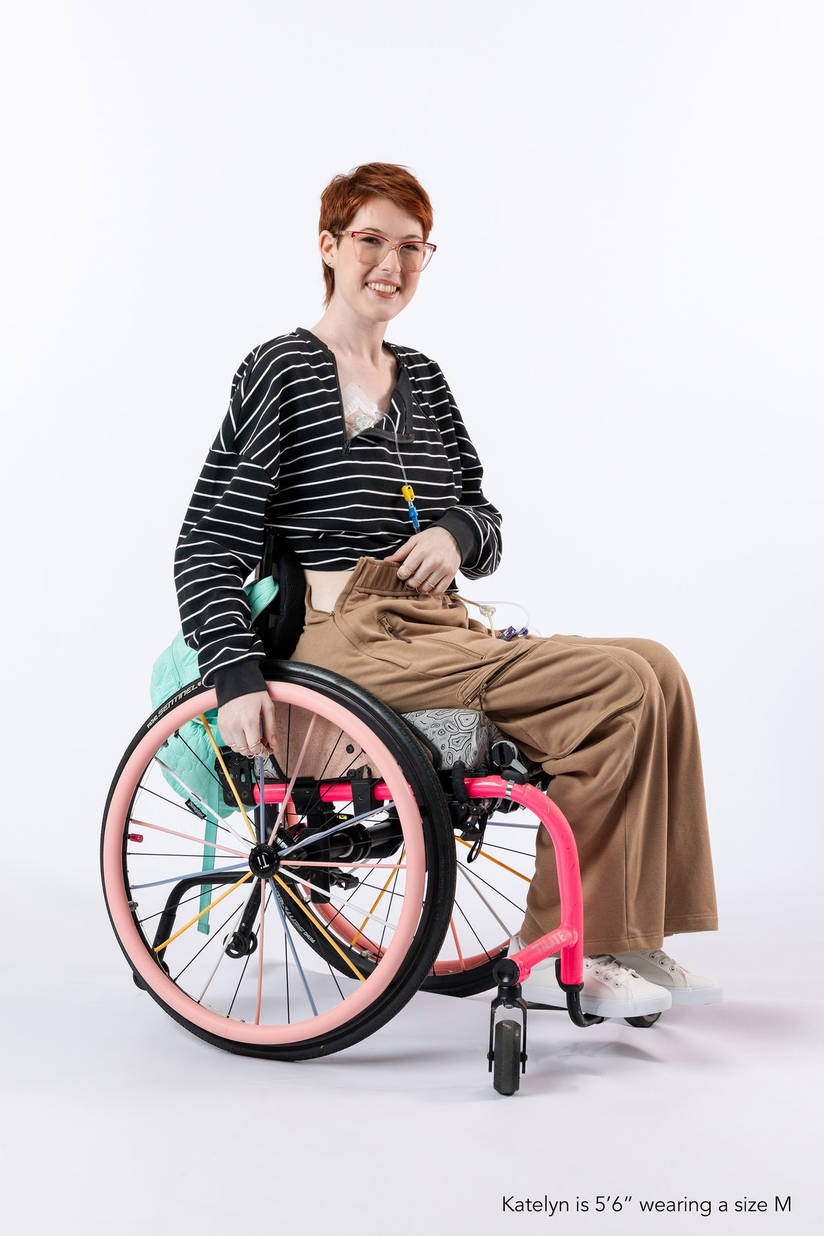 Woman in wheelchair wearing zipper access tee and  cargo pant.  Text reads "Katelyn is 5'6" wearing a size M."