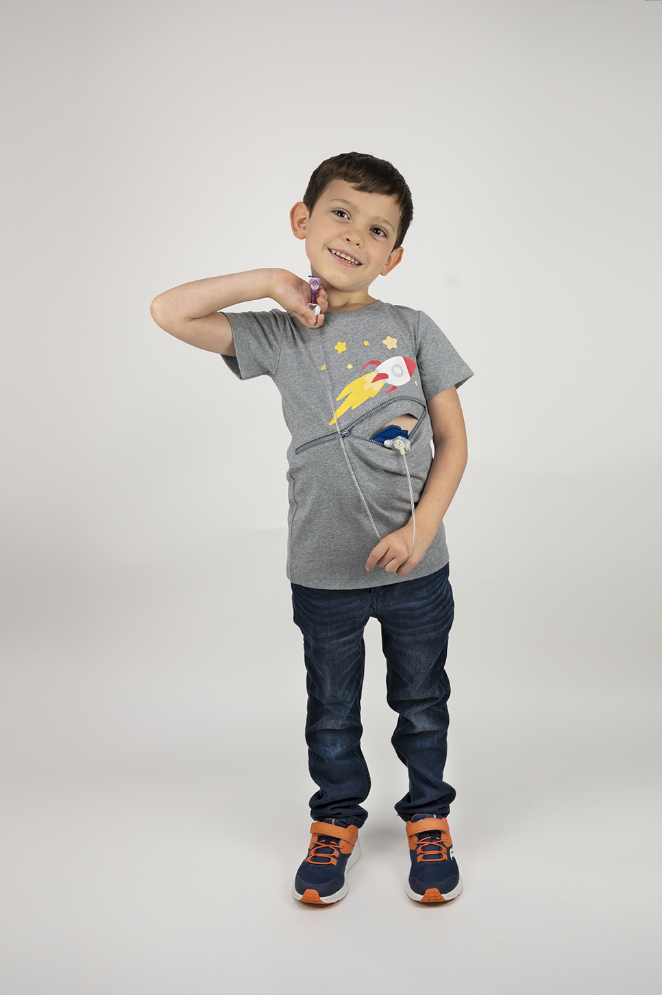 Boy standing Gray Spaceship G-tube zip shirt with zipper for abdominal access open to show g-tube pad