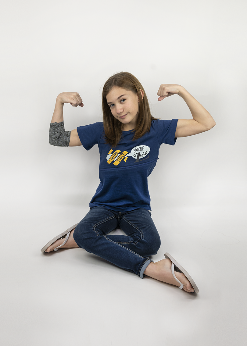 Girl sitting with arms flexed wearing Royal Blue Spoonie for Life G-tube zip shirt with zipper for abdominal access
