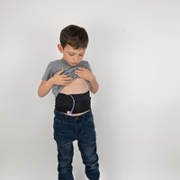 Child standing wearing black waistband with feeding tube visible